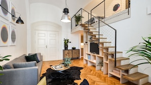 A modern living room with a grey sofa, a black leather rug, and a wooden staircase. - Lazenska N4 (Prague)