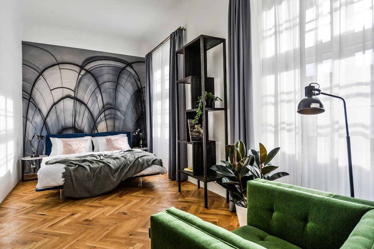 A modern bedroom with a bed, a green armchair, a floor lamp, and a plant.