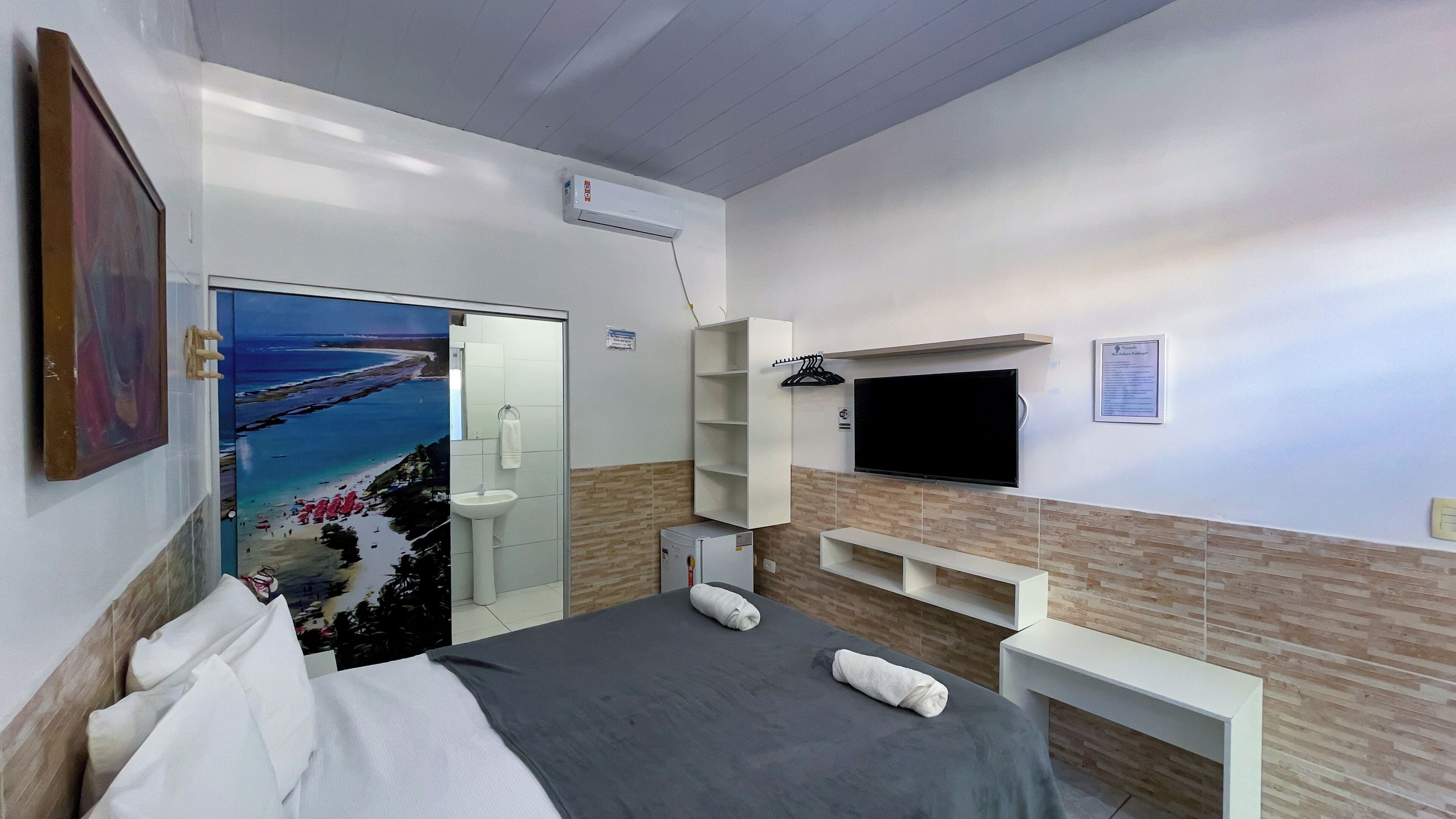 Une chambre d’hôtel avec un lit, une télévision, un tableau et une salle de bain équipée d’un lavabo et d’un miroir.
