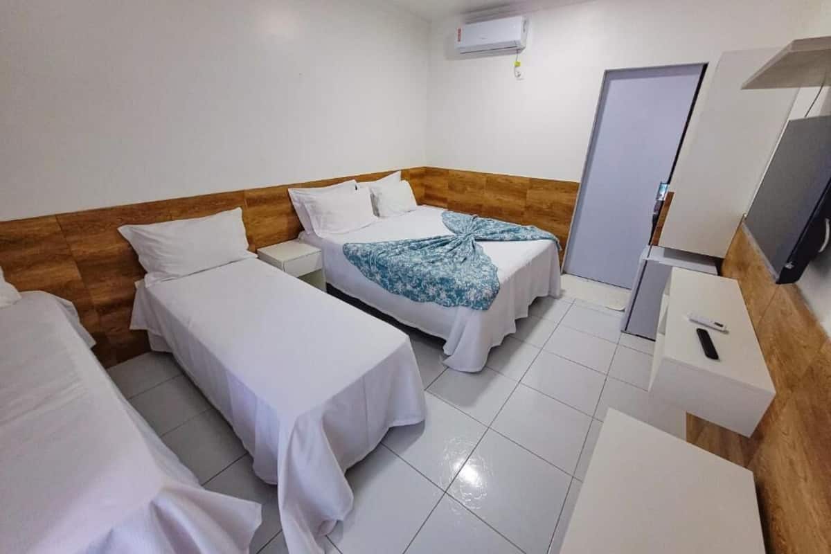 A hotel room with two single beds, a wooden headboard, a white air conditioning unit, a door, and a small table with a remote control.