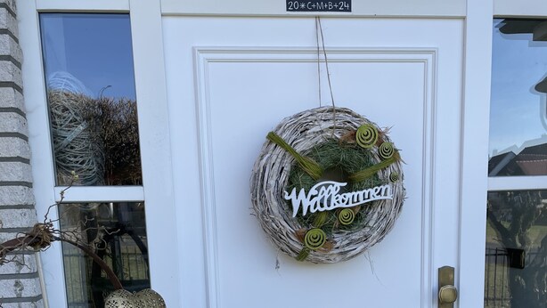 A white door with a 'Welcome' sign, a small tree sculpture, and a mailbox.
