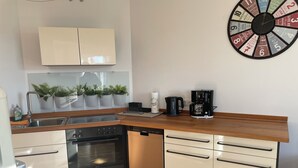 A modern kitchen with a dishwasher, oven, and sink. There are potted plants on the windowsill and a coffee maker on the counter.