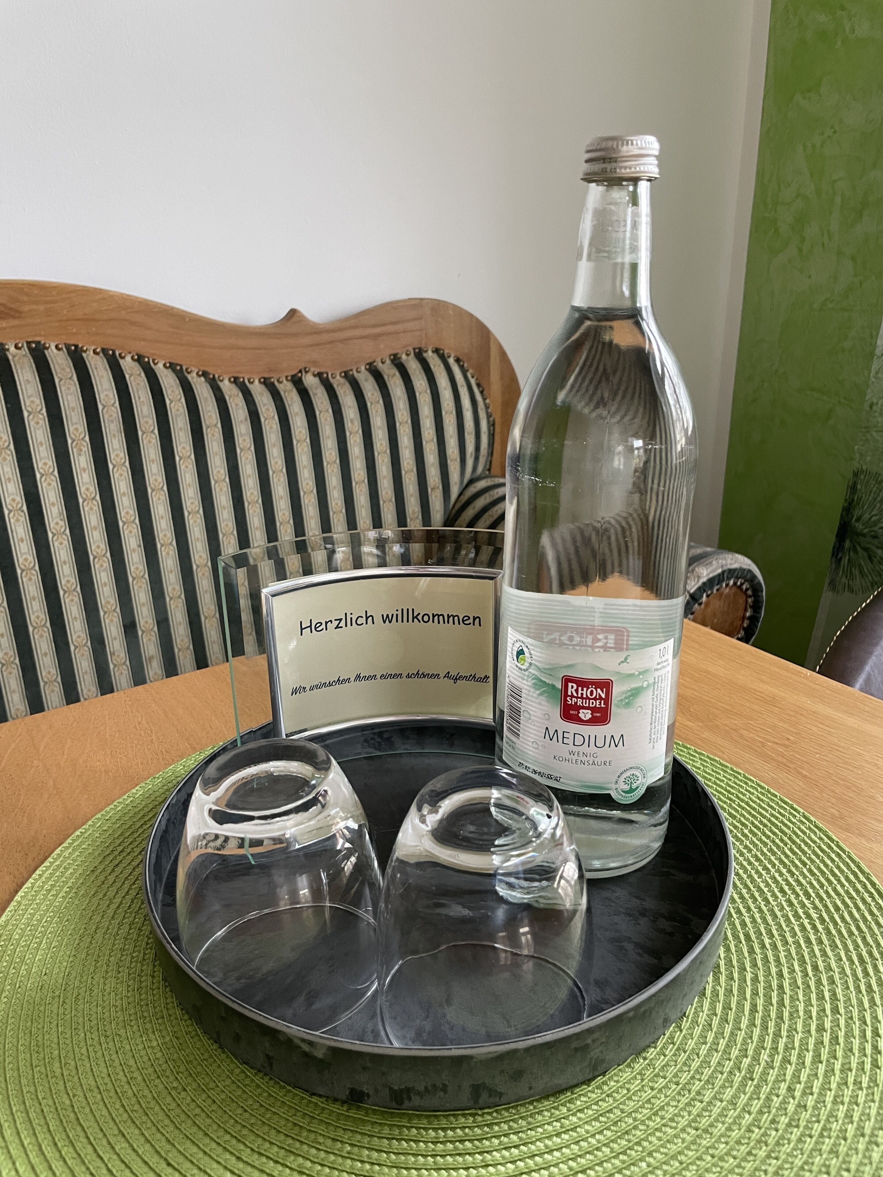 A tray with a bottle of Rhön Sprudel, three glasses, and a welcome card on a table.