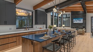 Une cuisine moderne dotée d’un grand îlot central, de tabourets de bar et d’un coin repas avec un canapé et une cheminée.