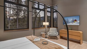 Une chambre moderne avec de grandes fenêtres, un lit, un bureau, une chaise et un téléviseur qui diffuse une image d’un skieur.