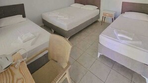Une chambre d’hôtel avec trois lits simples, une petite table, une chaise, un ventilateur de plafond et un appareil de climatisation.