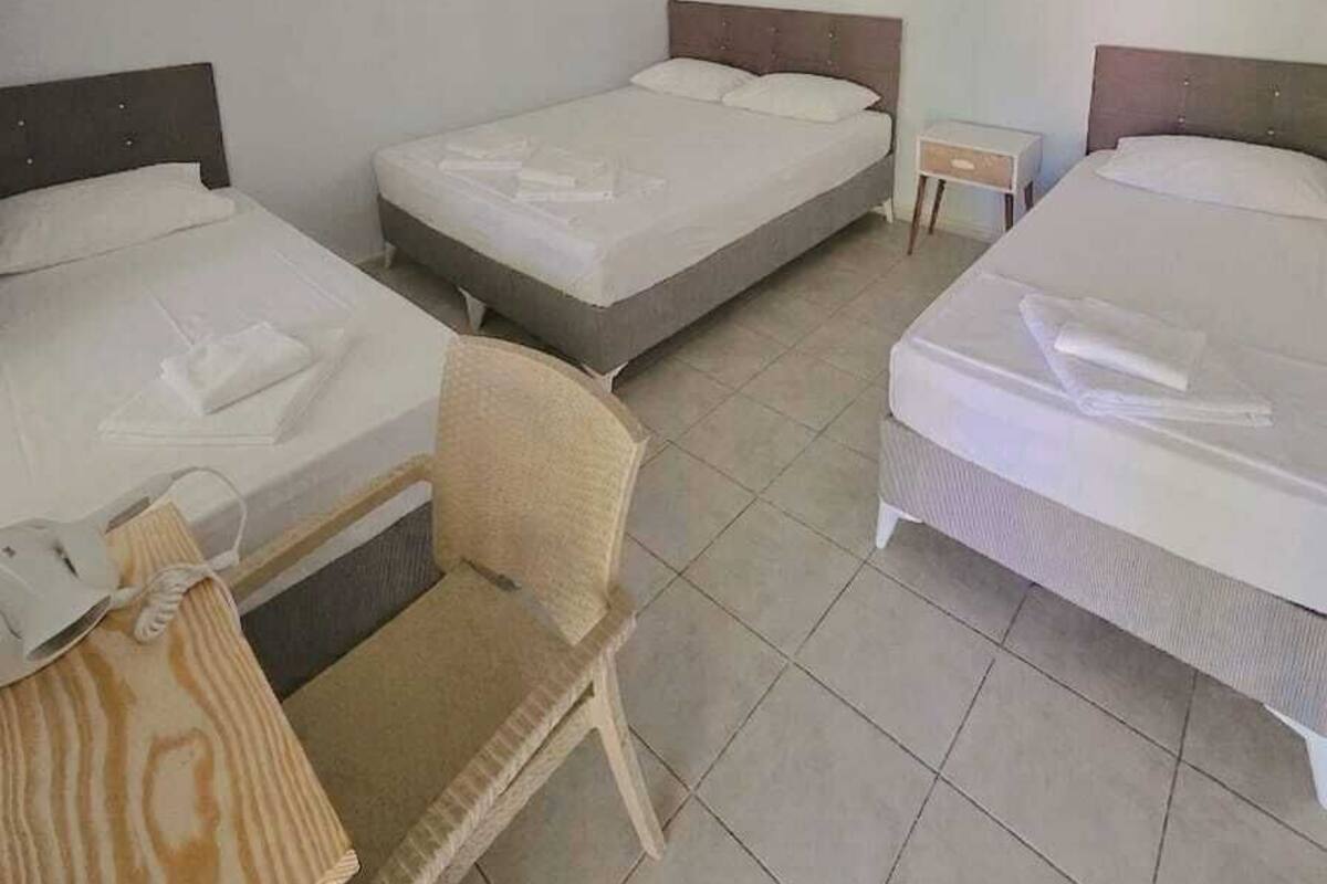 A hotel room with three single beds, a small table, a chair, a ceiling fan, and an air conditioning unit.