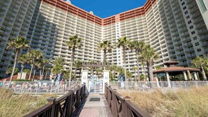 A high-rise hotel with multiple balconies, palm trees, and a gated entrance. - Shores of Panama #1129 | Stunning Views + Fun On-Site Amenities! (Panama City Beach)