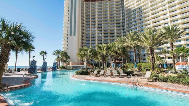 A hotel with a large pool area, palm trees, and a view of the ocean. - Shores of Panama #1129 | Stunning Views + Fun On-Site Amenities! (Panama City Beach)