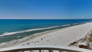 A beach view with a clear sky, calm sea, and a sandy shore with people and umbrellas. - Shores of Panama #1129 | Stunning Views + Fun On-Site Amenities! (Panama City Beach)