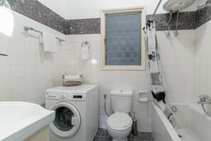 A compact bathroom with a washing machine, toilet, and bathtub.