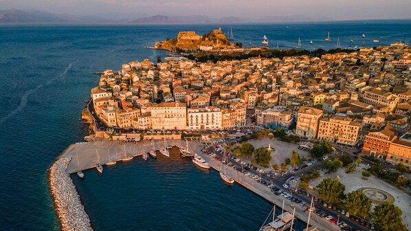 An aerial view of a coastal city with historic buildings, a fortified structure, and a marina.
