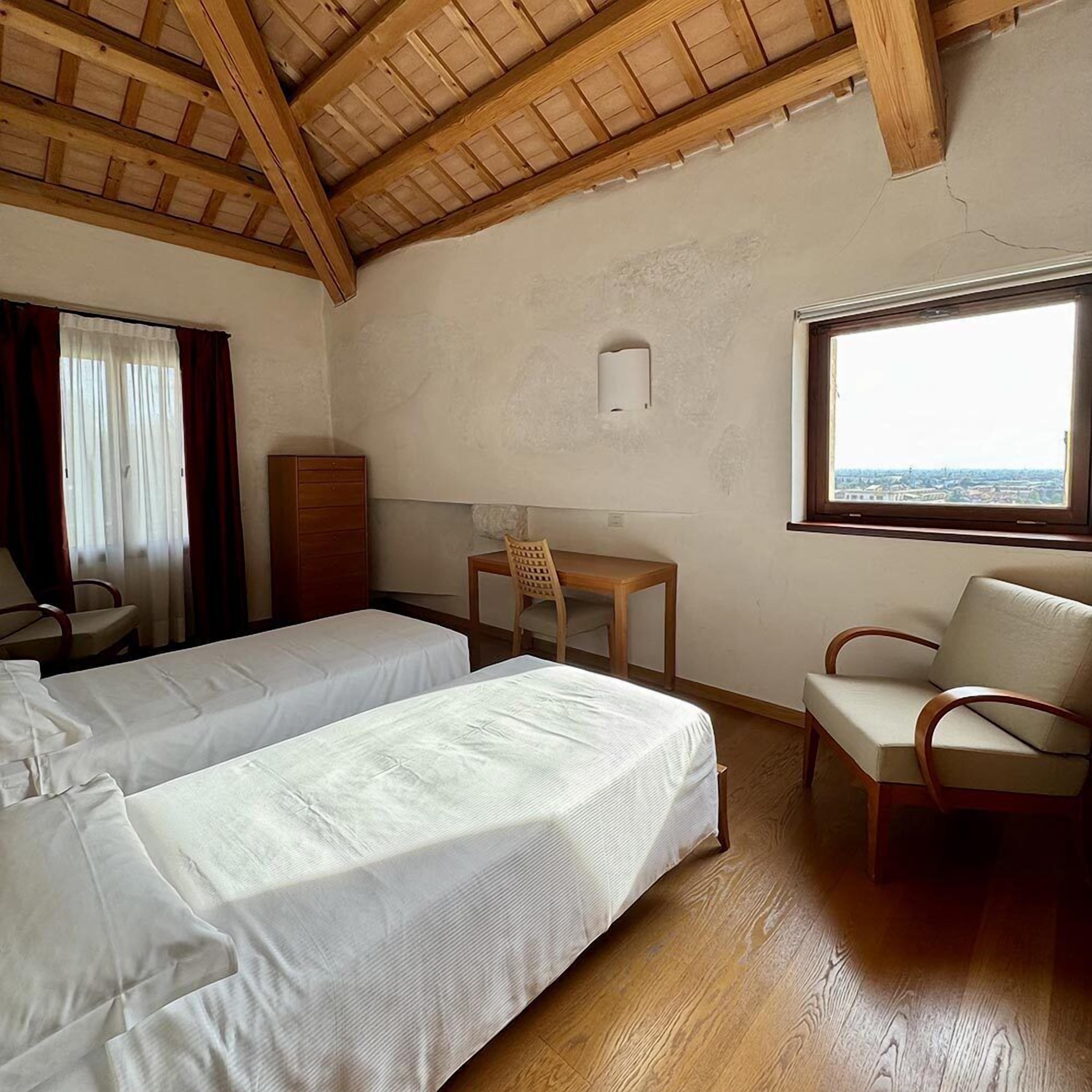 A room with two beds, a desk, a chair, and a window with a view.