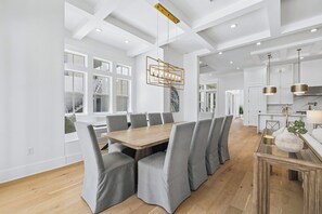 A modern dining area with a wooden table, grey upholstered chairs, and a pendant light. - 30A White Dunes Retreat-Luxury Compound, Large Private Pool and Outdoor Space (Santa Rosa Beach)