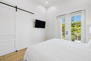 A bedroom with a bed, a television mounted on the wall, and a sliding glass door leading to an outdoor area. - 30A White Dunes Retreat-Luxury Compound, Large Private Pool and Outdoor Space (Santa Rosa Beach)