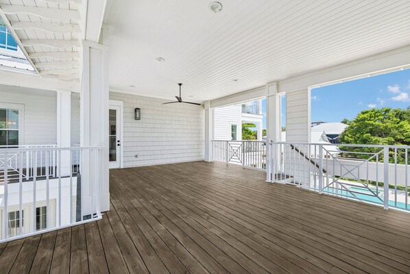 A covered wooden deck with a ceiling fan, white railings, and a view of a swimming pool.