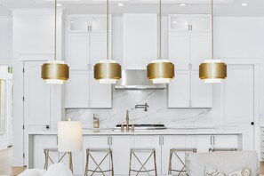 A modern kitchen with white cabinetry, a marble countertop, and gold-toned pendant lights.