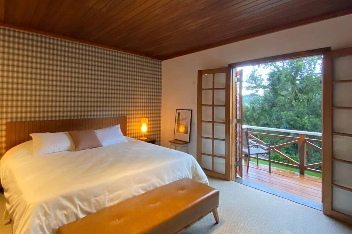 A bedroom with a large bed, a bench, a checkered wall, and a view of the outdoors through a sliding door.