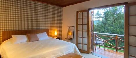 A bedroom with a large bed, a bench, a checkered wall, and a view of the outdoors through a sliding door.
