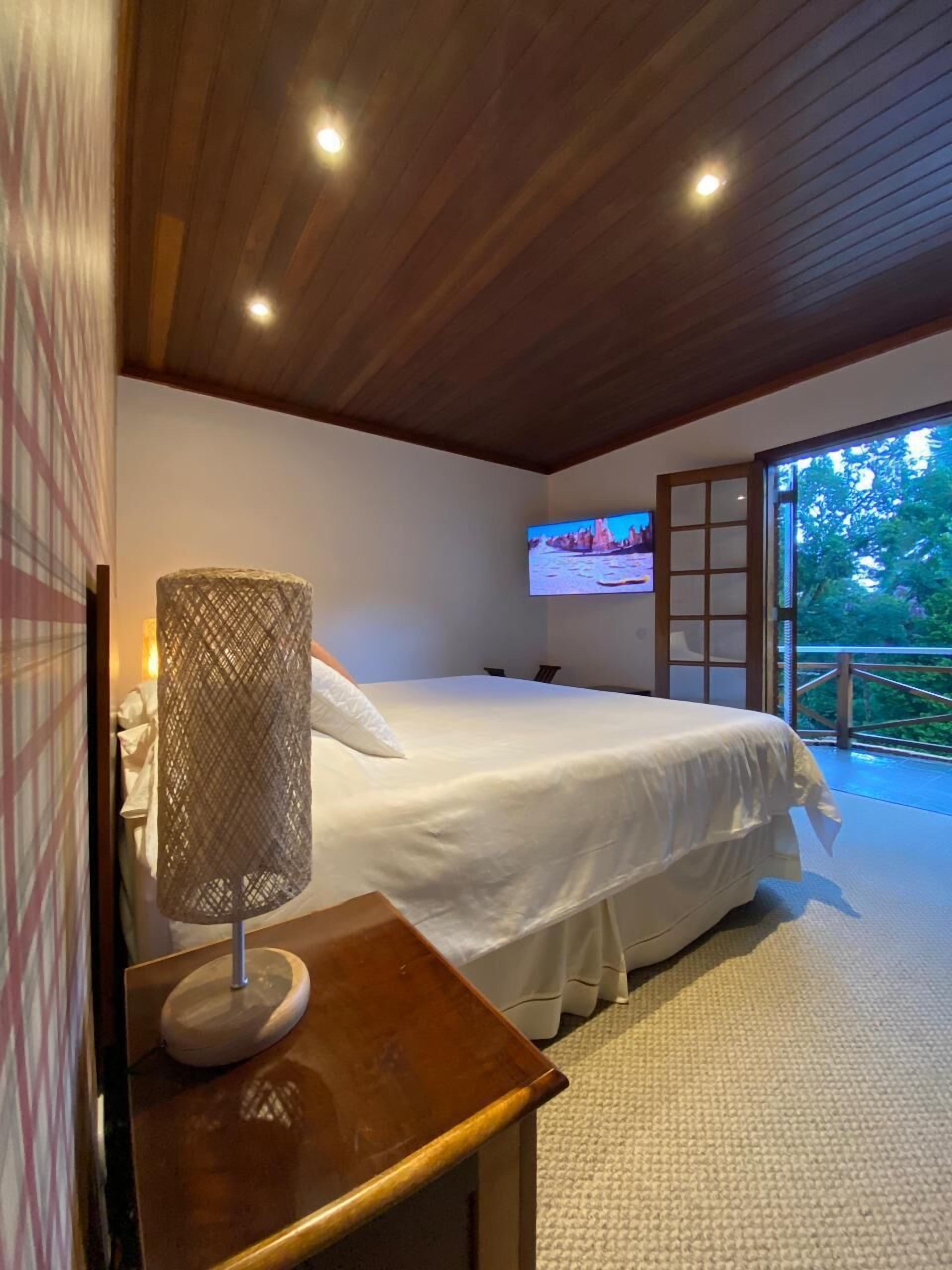 Quarto com cama, luminária, televisão e vista para o exterior.