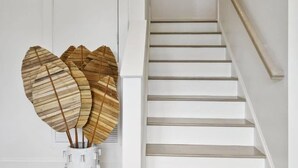 A staircase with white steps and a wooden handrail, leading to a door with a decorative hat hanging on the wall above it. - 7BR Coastal Retreat | Heated Pool & Game Area (Bay St. Louis)