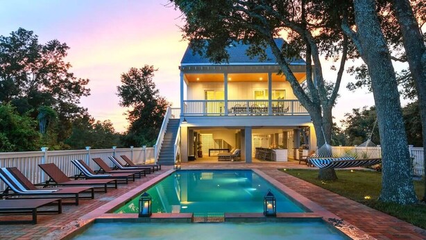 A two-story house with a swimming pool, outdoor seating, and a hammock. - 7BR Coastal Retreat | Heated Pool & Game Area (Bay St. Louis)