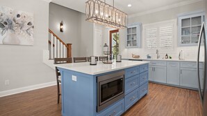 A kitchen with a central island, blue cabinets, a stainless steel oven, and a pendant light. - Brand New Home, Sleeps 10, Pool and Screened-in Porch with TV! (St Simons Island)