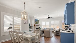 A spacious living area with a dining table, chairs, and a kitchen area with a blue cabinet. - Brand New Home, Sleeps 10, Pool and Screened-in Porch with TV! (St Simons Island)