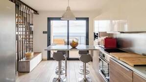 A modern kitchen with a large window, a dining area with bar stools, and a view of the sea.