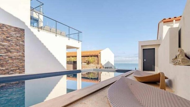 A modern pool area with clear blue water, a stone wall, and a lounge chair.