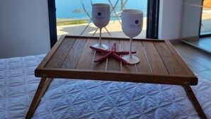 A bed with a wooden headboard, a wooden table with two wine glasses and a starfish, and a view of a balcony with a table and chairs.