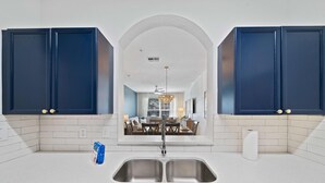 Une cuisine avec des meubles de couleur bleu foncé, un plan de travail blanc et un évier à deux bacs.