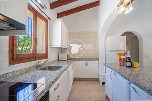 Une cuisine dotée de plans de travail en granit, de meubles blancs, d’un four encastré et d’une fenêtre donnant sur un paysage verdoyant.