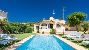Une piscine avec des chaises longues, une maison équipée d’une antenne parabolique et un ciel d’un bleu limpide.