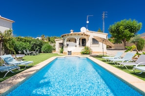 Una piscina con sillas de descanso, una casa con antena parabólica y un cielo azul despejado.