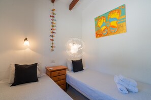 A bedroom with two beds, a nightstand, a wall-mounted light, a decorative fish string, and a colorful artwork. - CostaBlancaDreams - Casa Colibri in Calpe (Calpe)