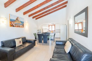 A living room with two black leather sofas, a dining table with chairs, a kitchen area, and a large mirror on the wall. - CostaBlancaDreams - Casa Colibri in Calpe (Calpe)