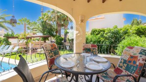 Un espace de restauration extérieur abrité, avec vue sur la piscine, comprenant une table ronde pour quatre personnes, entourée de chaises aux couleurs vives.