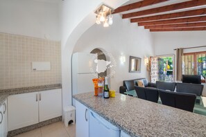 A kitchen with white cabinets, a granite countertop, and a dining area with black chairs. - CostaBlancaDreams - Casa Colibri in Calpe (Calpe)