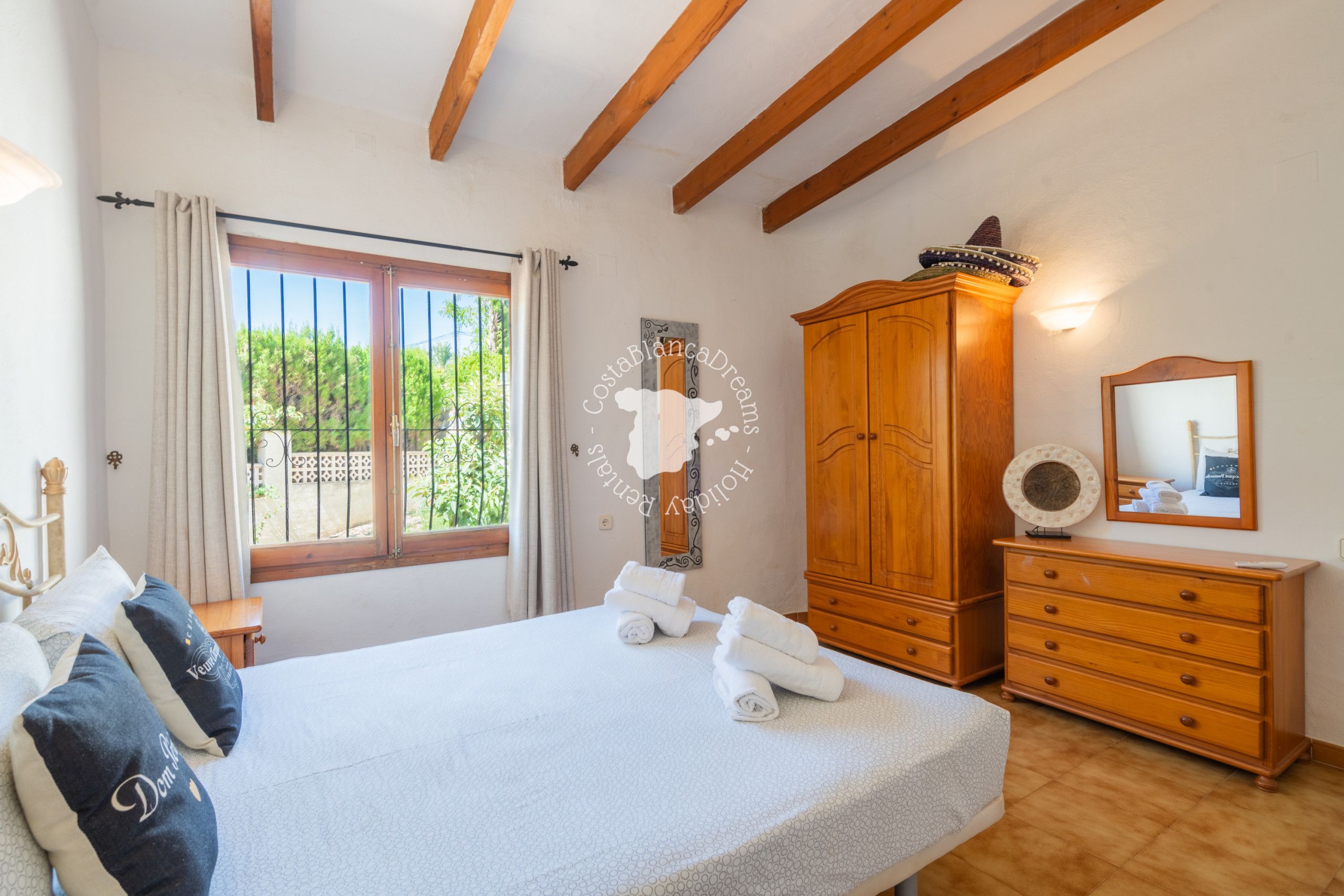 Une chambre à coucher avec un lit, une armoire en bois et une fenêtre avec des rideaux.
