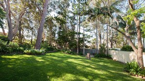 A well-maintained garden with a variety of trees and shrubs, a neatly trimmed lawn, and a wooden fence. - Vitamin Sea is pet friendly (Mollymook)
