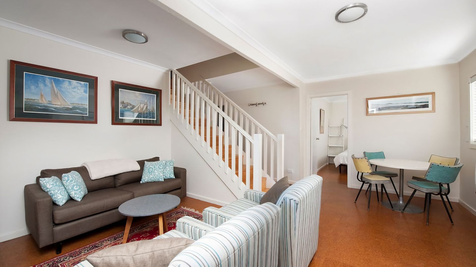 A living room with a sofa, a round coffee table, a striped sofa, a dining area with a table and chairs, and a staircase.
