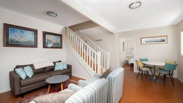 A living room with a sofa, a round coffee table, a striped sofa, a dining area with a table and chairs, and a staircase.