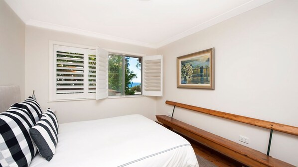 A bedroom with a bed, a bench, a painting, and a window with shutters. - Vitamin Sea is pet friendly (Mollymook)