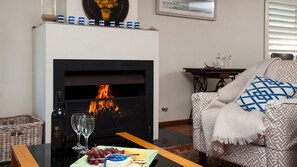 A living room with a fireplace, a table with a plate of food, glasses, and a bottle. - Vitamin Sea is pet friendly (Mollymook)