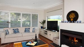 A living room with a sofa, coffee table, TV, fireplace, and a view of the outdoors. - Vitamin Sea is pet friendly (Mollymook)