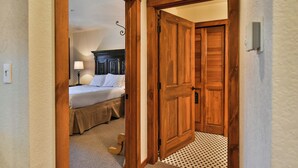 Een slaapkamer met een bed, een bedlampje en een houten deur naar een andere kamer.