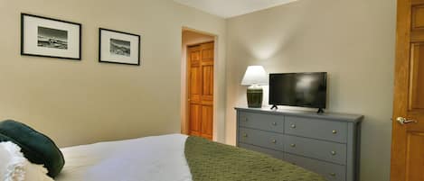 A bedroom with a bed, a dresser with a TV, and two framed pictures on the wall.