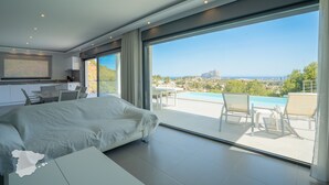 Een moderne slaapkamer met een groot bed, een bureau en uitzicht op een zwembad en de stad.