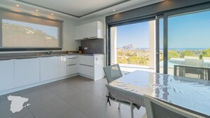 Een moderne keuken met witte kastjes, een groot raam en uitzicht op zee.